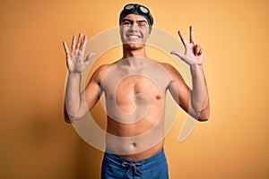 Young handsome man shirtless wearing swimsuit and swim cap over isolated yellow background showing and pointing up with fingers