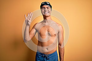 Young handsome man shirtless wearing swimsuit and swim cap over isolated yellow background showing and pointing up with fingers