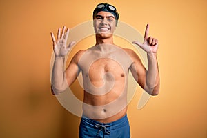 Young handsome man shirtless wearing swimsuit and swim cap over isolated yellow background showing and pointing up with fingers