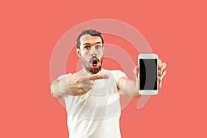 Young handsome man showing smartphone screen isolated on coral background in shock with a surprise face