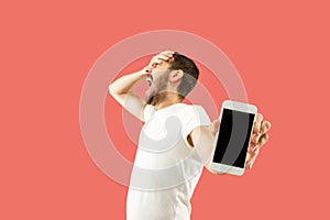 Young handsome man showing smartphone screen isolated on coral background in shock with a surprise face