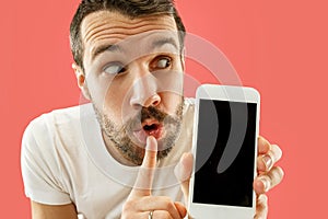 Young handsome man showing smartphone screen isolated on coral background in shock with a surprise face