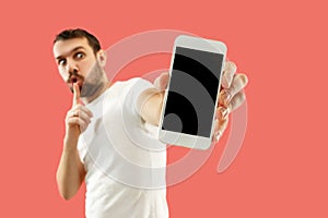 Young handsome man showing smartphone screen isolated on coral background in shock with a surprise face