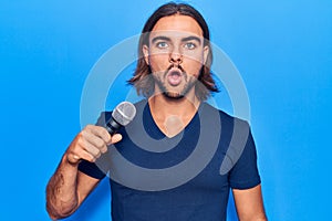 Young handsome man singing song using microphone scared and amazed with open mouth for surprise, disbelief face