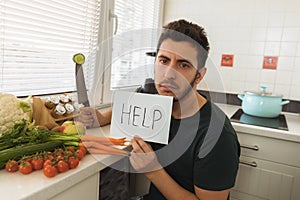 A young handsome man sits in the kitchen with a sad face and asks for help.