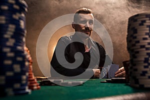 Young handsome man sitting behind poker table with cards and chips