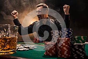 Young handsome man sitting behind poker table with cards and chips