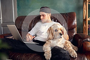 Young handsome man sitting and working at home with his cute dog. Cozy office workplace, remote work, online learning