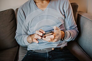 Young handsome man sitting at home on sofa and using mobile phone. Men holding smartphone hands and typing text message.