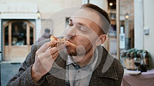 Young handsome man sitting in Italian restaurant and eating pizza. Hungry male enjoying the appetite food.