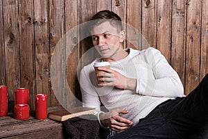 Young handsome man sitting near wood wall drinking coffee and reading book