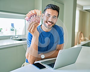 Young handsome man smiling happy holding south african rands banknotes at home