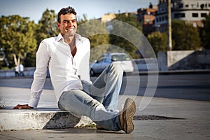 Young handsome man smiling sitting on the ground on sidewalk street. Outdoor