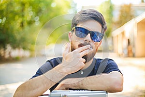 Young handsome man smokes with his hands on vintage tape recorder