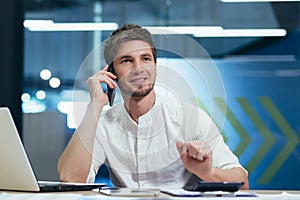 Young handsome man, specialist working in the office at the desk. Talking on a mobile phone with customers, with bank, with