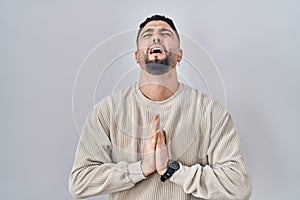 Young handsome man standing over isolated background begging and praying with hands together with hope expression on face very