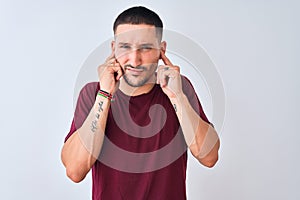 Young handsome man standing over isolated background covering ears with fingers with annoyed expression for the noise of loud