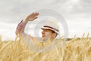 Young handsome happy man standing in wheat field spreading his arms up