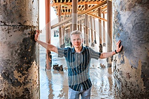 Young handsome man stands under a wooden pier on Malibu beach, California