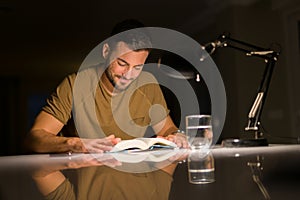 Young handsome man studying at home, reading a book at night