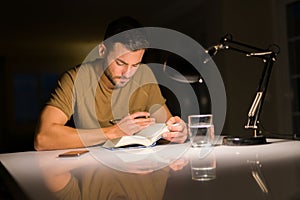 Young handsome man studying at home, reading a book at night