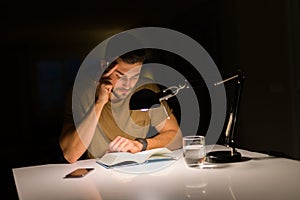 Young handsome man studying at home, reading a book at night