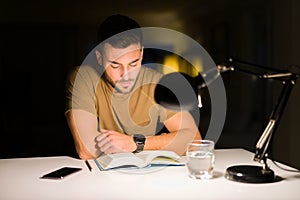 Young handsome man studying at home, reading a book at night