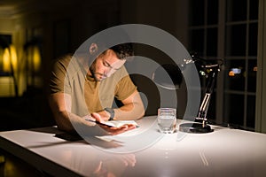 Young handsome man studying at home, reading a book at night