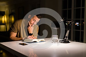 Young handsome man studying at home, reading a book at night