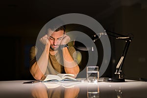 Young handsome man studying at home very bored and stressful reading a book at night