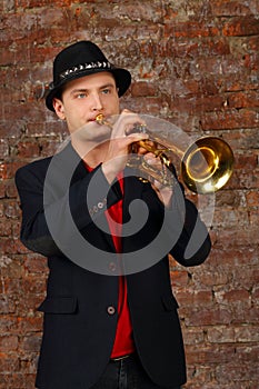 Young handsome man in suit and hat plays trumpet