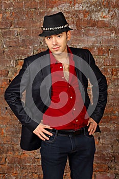 Young handsome man in suit and hat poses in studio