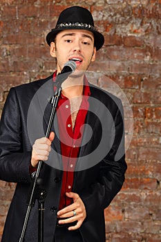 Young handsome man in suit and hat sings into photo
