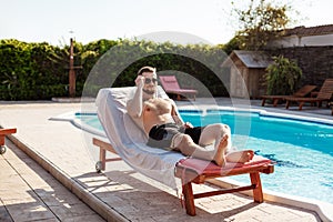 Young handsome man sunbathing, lying on chaise near swimming pool.