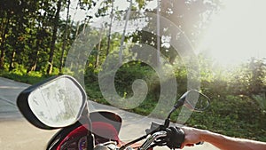 Young handsome man in sunglasses driving motorbike on tropical sunny road through the sun with beautiful lens flare