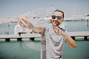 Young handsome man in sunglasses take selfie mobile phone pointer on camera on yacht harbor on background. travel concept