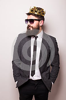 Young handsome man in sunglasses wearing suit and crown keeping hand on his jacket