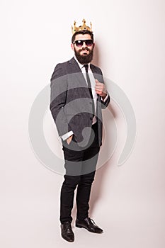 Young handsome man in sunglasses wearing suit and crown keeping hand on his jacket