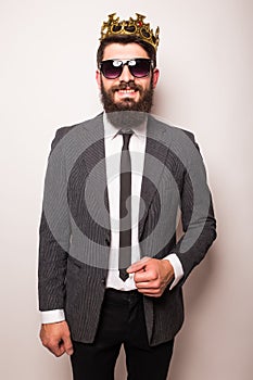 Young handsome man in sunglasses wearing suit and crown keeping hand on his jacket