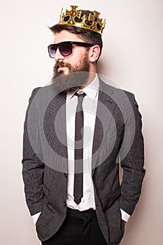 Young handsome man in sunglasses wearing suit and crown keeping hand on his jacket