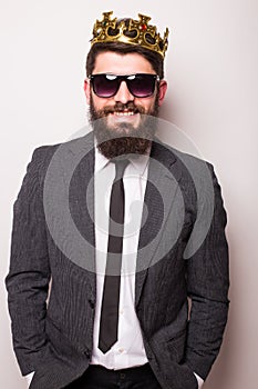 Young handsome man in sunglasses wearing suit and crown keeping hand on his jacket while standing