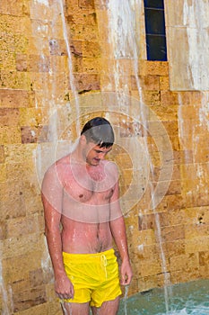 Young handsome man taking outdoor shower like a waterfall at the