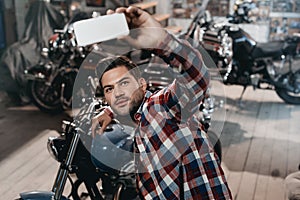 young handsome man taking selfie on smartphone with classic motorcycle