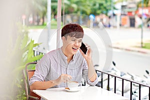 Young handsome man talking on the mobile phone while sitting in cafe outdoor