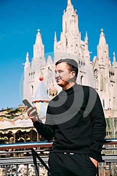 Young handsome man talking via headset standing in front of Tibidabo church. Travel concept photo