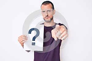 Young handsome man with tattoo holding question mark pointing with finger to the camera and to you, confident gesture looking