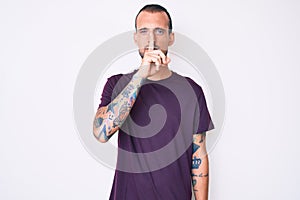 Young handsome man with tattoo wearing casual clothes asking to be quiet with finger on lips