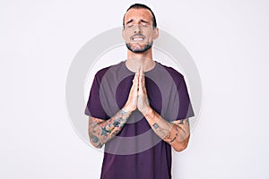 Young handsome man with tattoo wearing casual clothes begging and praying with hands together with hope expression on face very