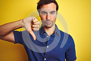 Young handsome man with tattoo wearing casual shirt standing over isolated yellow background with angry face, negative sign