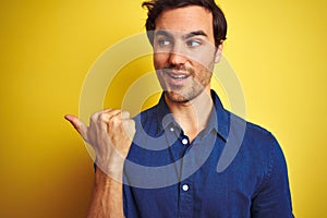 Young handsome man with tattoo wearing casual shirt standing over isolated yellow background pointing and showing with thumb up to